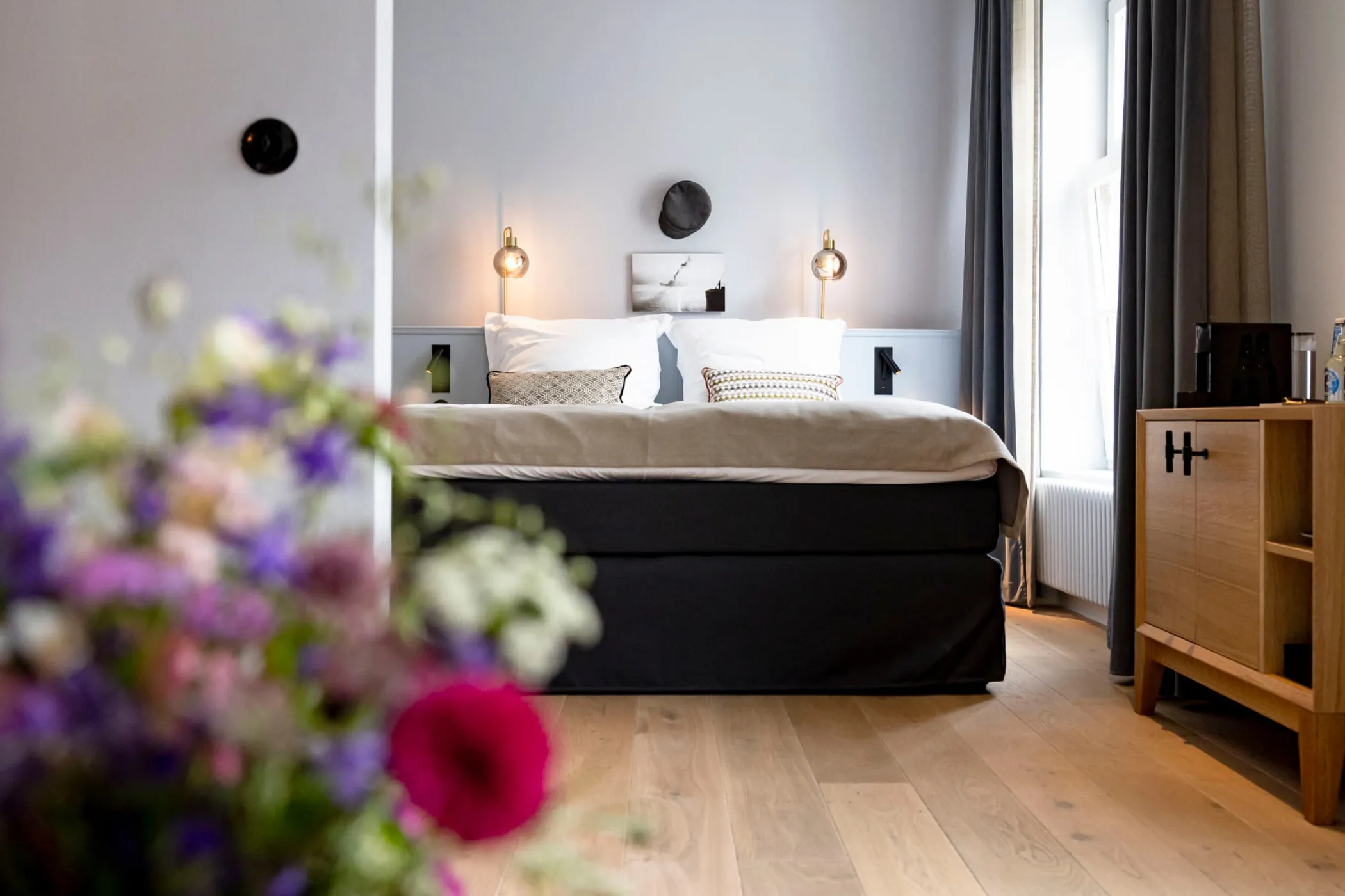 Zimmer im Boutiquehotel Petuh, im Vordergrund ein Strauß bunter Sommerblumen, dahinter das gemachte Bett am Fenster