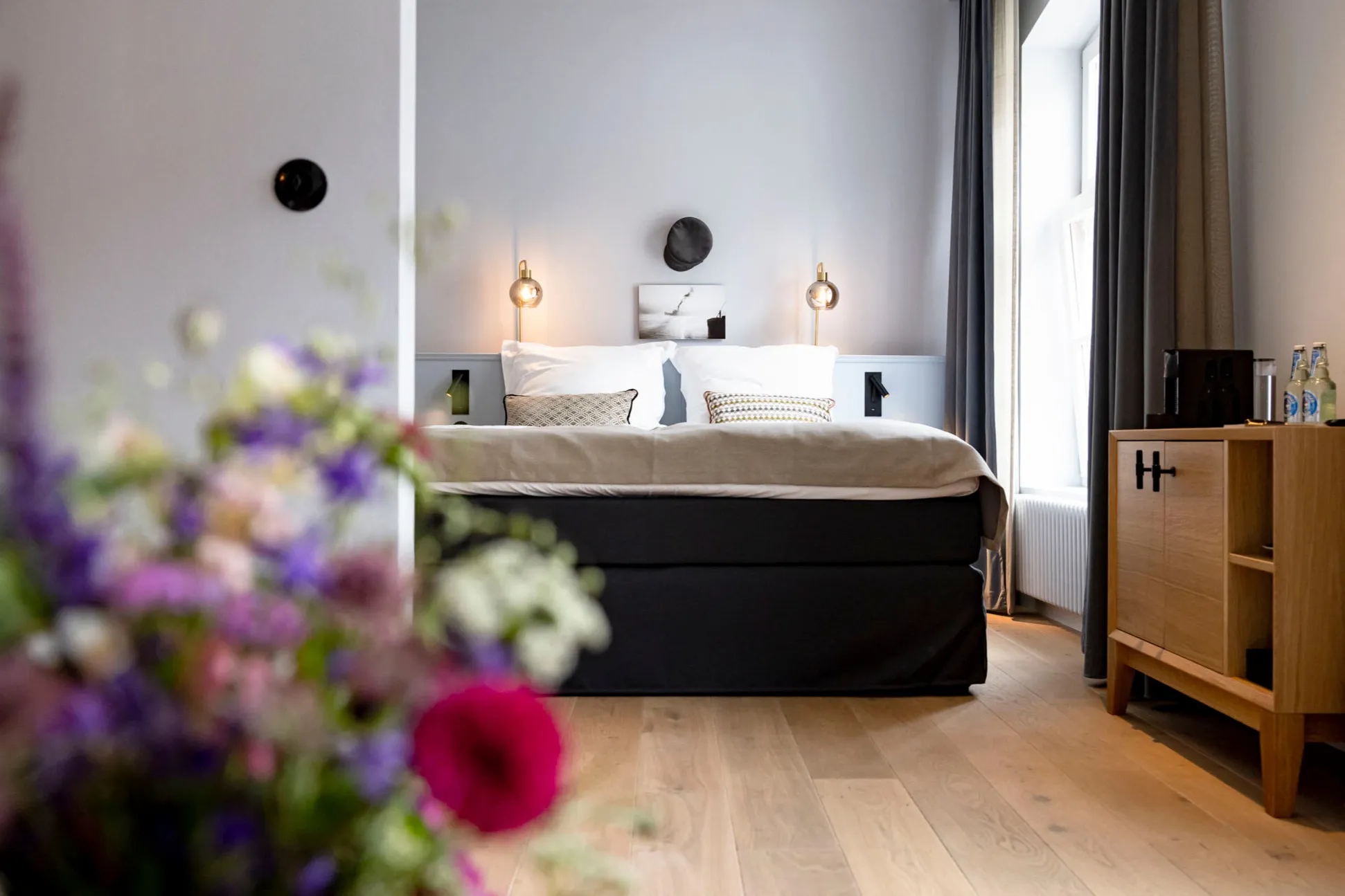 A room at Boutiquehotel Petuh, a bunch of summer flowers in the foreground, the made bed by the window behind